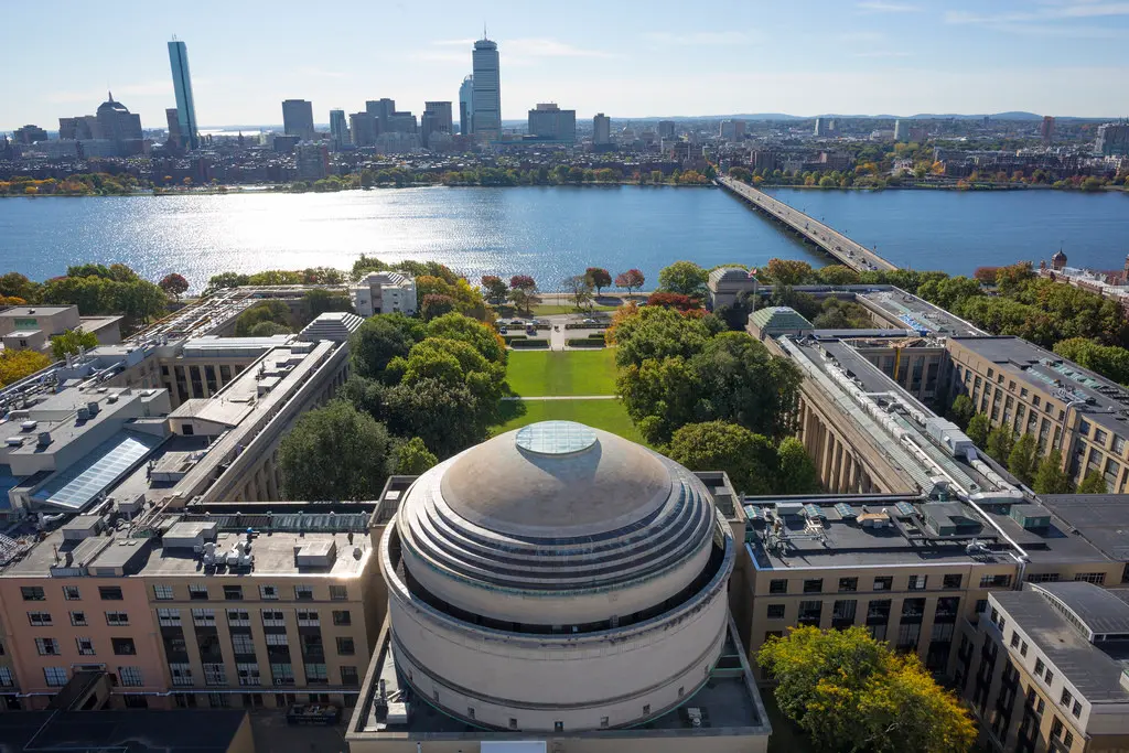 Aerial view of the MIT campus, above the rotunda, on a sunny day, looking across the Charles River to the city beyond.